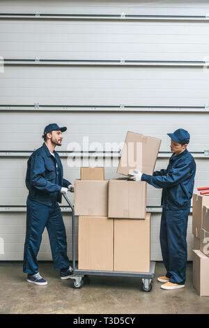 Zwei movers in Uniform Transport von Kartons auf Hand-Lkw im Lager mit Kopie Raum Stockfoto