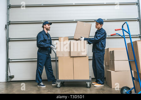 Zwei movers in Uniform Transport von Kartons auf Hand-Lkw im Lager mit Kopie Raum Stockfoto