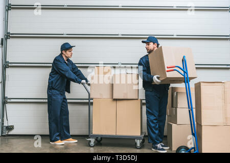 Zwei movers in Uniform sich einander beim Transport Kartons mit hand Trucks im Lager Stockfoto