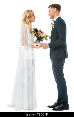 Lächelnd Braut im weissen Brautkleid und Bräutigam im schwarzen Anzug, Hände halten und bei jeder anderen sich isoliert auf weißem Stockfoto