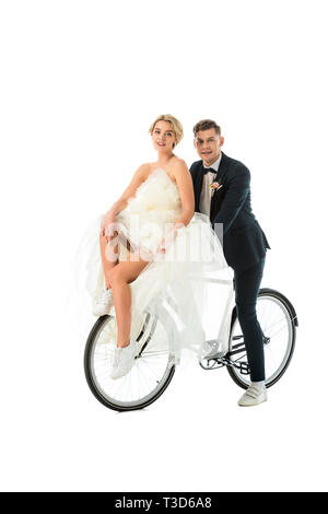 Schöne Braut im Brautkleid und gutaussehenden Bräutigam sitzen auf dem Fahrrad isoliert auf weißem Stockfoto