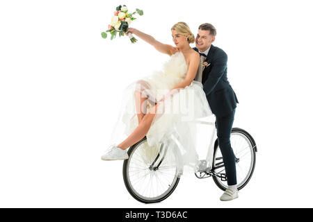 Schöne Braut Holding wedding bouquet in der erhobenen Hand, während auf dem Fahrrad sitzen zusammen mit Bräutigam isoliert auf weißem Stockfoto