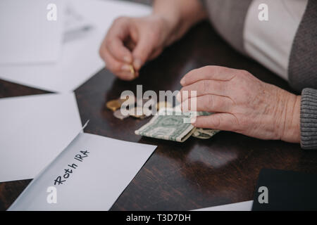7/8-Ansicht von Paar Frau zählen Geld in der Nähe von Umschlag mit "Roth IRA' Schriftzug Stockfoto