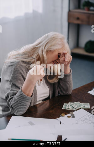 Müde senior Frau am Tisch sitzen und mit Kopfschmerzen und zählen Sie das Geld zu Hause Stockfoto