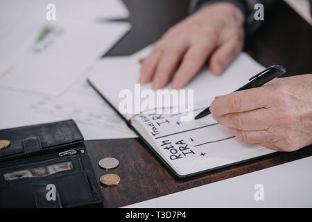 7/8-Ansicht der älteren Frau schreiben in Notebook mit Roth IRA und traditionelle ira Worte Stockfoto