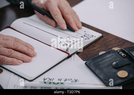 7/8-Ansicht der älteren Frau mit Stift in der Nähe von Notebook mit Roth IRA und traditionelle ira Worte Stockfoto