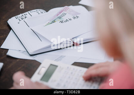 7/8-Ansicht der älteren Frau, Umschlag mit "Roth IRA" Schriftzug, Geld und Notebook Stockfoto
