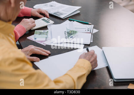 Senior Paar am Tisch sitzen mit Schreibarbeit, Umschlag mit 'Roth IRA" Schriftzug und Geld Stockfoto