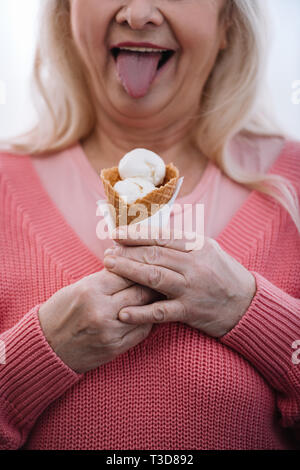 7/8-Ansicht der älteren Frau klemmt die Zunge heraus und halten Eis Stockfoto