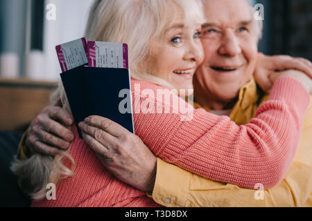 Lächelnd senior Paar umarmen und Holding Air Tickets mit Pässen zu Hause Stockfoto