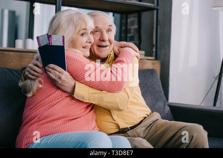 Gerne älteres Paar umarmen und Holding Air Tickets mit Pässen zu Hause Stockfoto