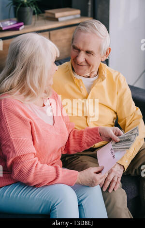 Lächelnd senior Paar hält Umschlag mit "Roth IRA" Schriftzug und Dollar Banknoten Stockfoto