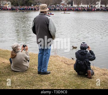 Zwei sitzende Kinder Aufnehmen von Bildern und einem Erwachsenen stehen, Sie beobachten die Zuschauer auf der anderen Seite des Sees. Swan parade Veranstaltung. Stockfoto