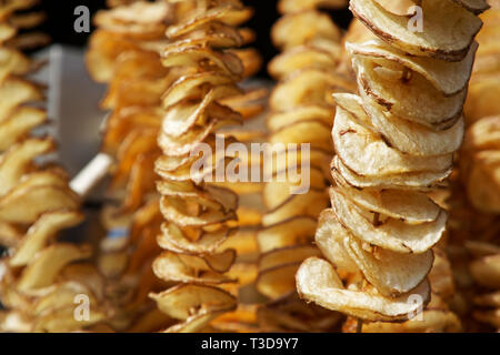 Fried Potato Chips auf Stick, Spirale Kartoffeln gebraten, auf Holzstäbchen, Spirale. Verkauf von Speisen auf dem Markt. Ungesunde fried Street Food Stockfoto