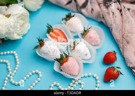 Frische Erdbeeren in Weiß und Rosa Schokolade liegen auf einem türkis Hintergrund Stockfoto