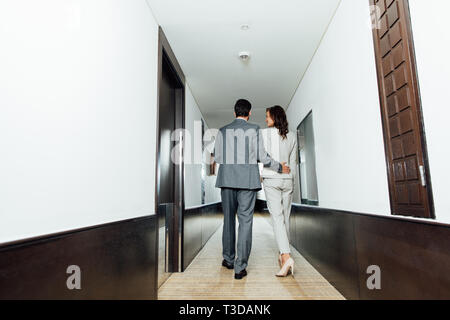 Rückansicht des zuversichtlich Geschäftsmann umarmen Geschäftsfrau, die in förmlichen tragen Sie beim Wandern im Hotel Flur Stockfoto