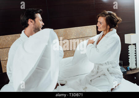 Freundliche Paar in Bademänteln in Kissenschlacht im Bett im Hotel Stockfoto