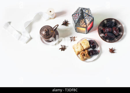 Gruß Ramadan Kareem Karte, Einladung. Bronze Platte mit Termine Obst, baklava Gebäck, Kaffee Tasse, leuchtende Laterne auf weißer Tisch. Iftar Abendessen. Eid Stockfoto