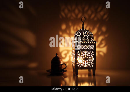 Silhouette von glühenden Marokkanischen dekorative Laterne mit Bronze Tee Tasse. Dekorative goldenen Schatten. Grußkarte, Einladung für die muslimischen heiligen Monat Rama Stockfoto