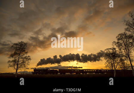 Dramatische malerische Seitenansicht der bewegten Vintage UK Dampfzug Silhouette in Sonnenuntergang, vorbei an Landschaft, die Dampf, Rauch puffend. Stockfoto