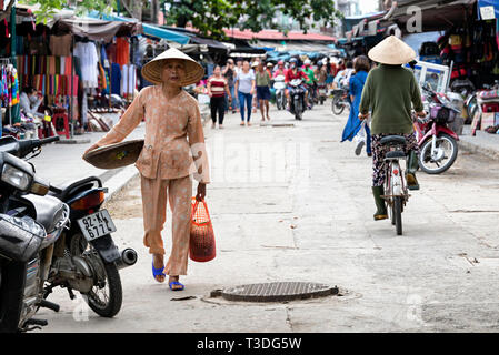 Vietnamesische Frau in traditioneller Kleidung zu Fuß rund um den Street Market in Hoi An, Vietnam Stockfoto