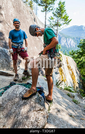 Ein Mann Band in ein kletterseil während bereit, ein Klettern zu führen, während sein Partner steht bereit zu sichern. Die wenig Rauch Bluffs, Squamis Stockfoto