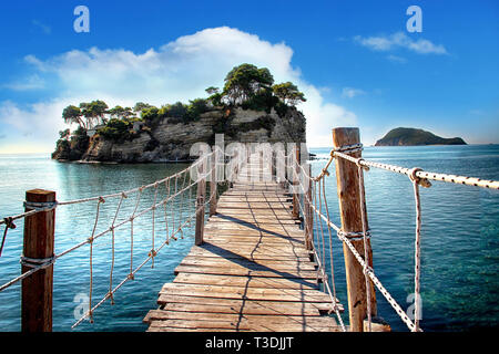 Die hölzerne Brücke mit Blick auf das Meer führt zu einer Insel mit Palmen. Stockfoto