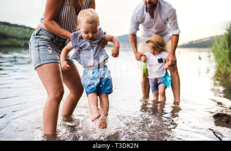 Ein Mittelteil von Familie mit zwei Kleinkindern Kinder draußen am Fluss im Sommer. Stockfoto