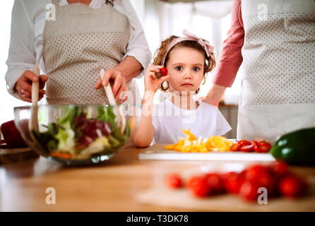 Ein kleines Mädchen mit Mutter und Großmutter zu Hause, Vorbereitung von Salat. Stockfoto