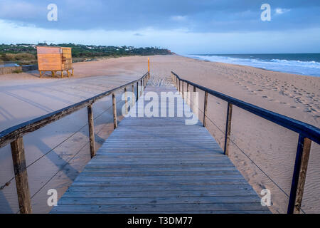 Auf der Suche einer geraden Holzterrasse weg mit hölzernen Geländer auf jeder Seite, die Bahn ist auf einem großen Geschwungenen Sandstrand und führt auf reine San Stockfoto