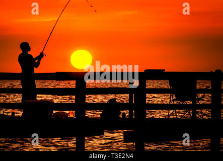 Ein Mann wird von der untergehenden Sonne silhouetted, wie Er fischt, 1. Juli 2013, in der Cedar Point Fishing Pier auf der Alabama Gulf Coast. Stockfoto