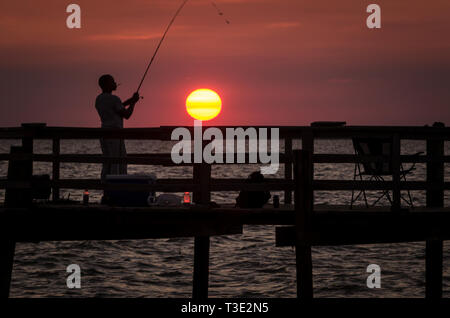 Ein Mann wird von der untergehenden Sonne silhouetted, wie Er fischt, 1. Juli 2013, in der Cedar Point Fishing Pier auf der Alabama Gulf Coast. Stockfoto