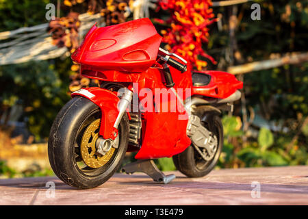 Ein isolierter closeup rot Spielzeug Motorrad mit warmen Farben - von vorne. Foto von einem Garten eingenommen hat. Stockfoto