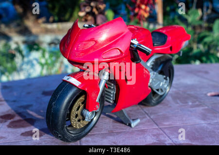 Ein isolierter closeup rot Spielzeug Motorrad mit kalten Farben. Foto von einem Garten eingenommen hat. Stockfoto