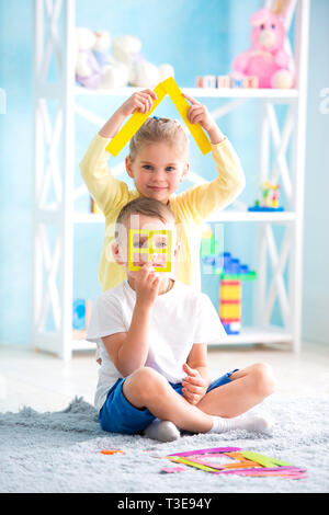 Ein kleines Mädchen mit ein Junge sitzt auf dem Boden und halten ein farbiges Papier Stockfoto