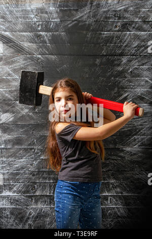 Kleines Mädchen schaukeln eine riesige langstieligen Hammer auf eine schmutzige dunkle Hintergrund Stockfoto