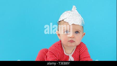 Baby in eine Folie Hut sitzt auf einem blauen Hintergrund Stockfoto