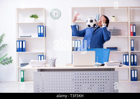 Junge gut aussehender Geschäftsmann mit Fußball im Büro Stockfoto
