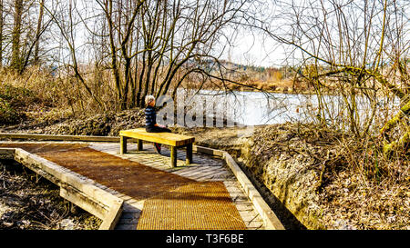 Ältere Frau ruht auf einer Holzbank, Wandern der Weg aus Pappel Bar bis hin zu 2-bit-Bar im Glen Valley Regional Park in der Nähe von Fort Langley, BC, Kanada Stockfoto