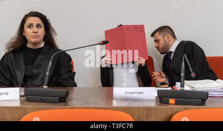 München, Bayern, Deutschland. 9. Apr 2019. Zu Beginn der Studie, der Angeklagte sitzt in den Gerichtssaal zwischen den Anwälten Sera Basay-Yildiz (l) und Ali Aydin (r) mit einem roten Datei Abdeckung vor ihrem Gesicht. Die Frau ist der Kriegsverbrechen und der Mitgliedschaft in einer terroristischen Vereinigung vorgeworfen. Sie und ihr Mann sind, sagte ein kleines Mädchen aus einer Gruppe von yeziden Kriegsgefangene als Slave im Sommer 2015 gekauft zu haben. Foto: Peter Kneffel/dpa Quelle: dpa Picture alliance/Alamy leben Nachrichten Stockfoto