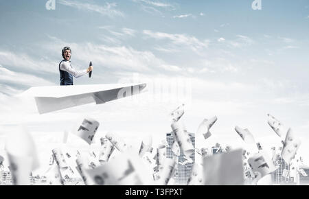 Aviator fahren Paper Plane über Business Center im blauen Himmel. Arbeiten mit Business Dokumentation. Papiere, die auf dem Hintergrund der Wolkenkratzer. Stockfoto