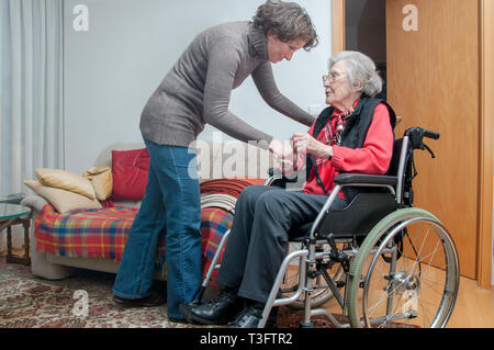 Junge Frau kümmert sich um die ältere Frau sitzt im Rollstuhl Stockfoto