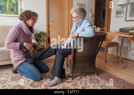 Junge. Frau helfen älteren Dame auf ihre Schuhe Stockfoto