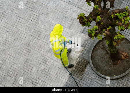 Blick von oben auf ein Arbeiter die Straße Gehweg mit Hochdruck Wasserstrahl reinigen. Öffentliche Wartungskonzept Stockfoto