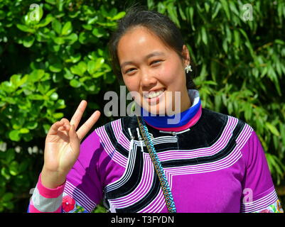 Junge chinesische Miao Frau (ethnische Minderheiten) trägt einen farbenfrohen traditionellen ethnischen Kleid und blinkt das V-Zeichen. Stockfoto
