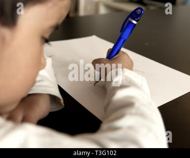 Junge Schrift auf weißem Papier mit blauen Stift auf einem Schwarzen Tisch mit Gesicht unfocused. Stockfoto