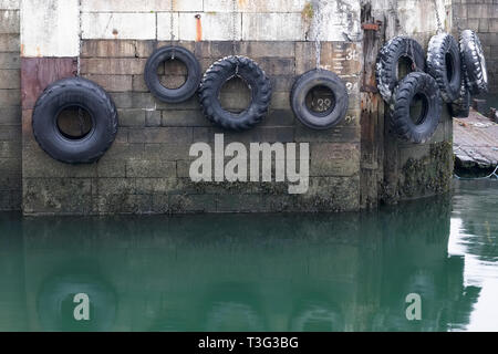Autoreifen hängen am Seil gegen die Hafenmauer in Port dock Schiffe und Boote zu schützen. Stockfoto
