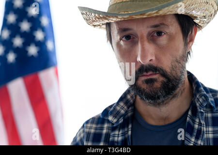 Schwere amerikanische Landwirt mit Kamera suchen, Portrait von erwachsenen männlichen Person mit Strohhut und Plaid Shirt mit USA-Flagge im Hintergrund Stockfoto