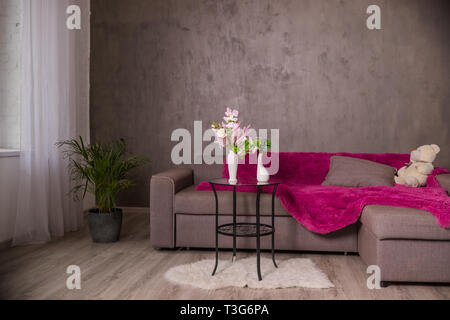 Skandinavische Wohnzimmer design interieur mit einem Sofa und einem runden Tisch mit Blumen Blumenstrauß. Braun Sofa mit Plaid, Kissen, Teddybär. Moderne Einrichtung Stockfoto