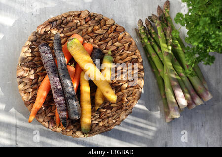 Eine Komposition von bunten Sorten von Karotten und Grünen frischen Spargel auf einem hellen Hintergrund mit Platz für Text. Horizontale Schuß Stockfoto